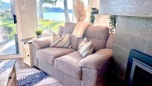 A living room with a sofa, a fireplace, a window with a view of trees, and a small table with a plant. - Seascape Oasis - 2BDRM - Ocean View - Kitchen (Nanoose Bay)