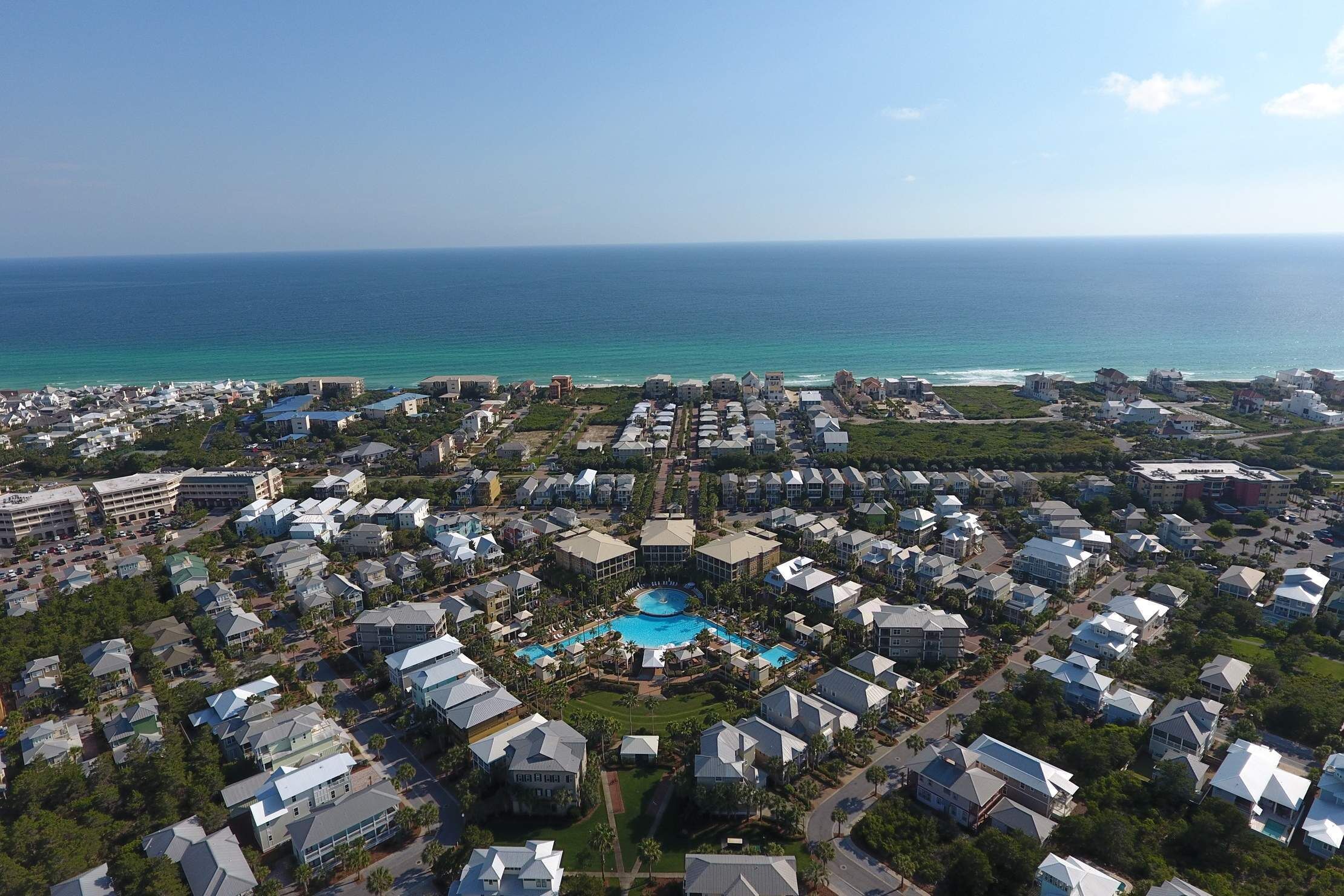 An aerial view of a coastal residential area with a central swimming pool surrounded by houses.