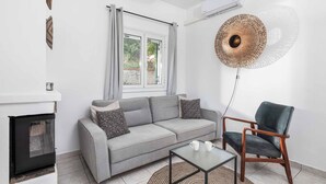 A modern living room with a grey sofa, a wooden chair, a glass coffee table, and a decorative wall lamp. - Villa Calma (Corfu)