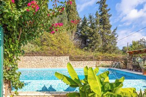 A swimming pool surrounded by lush greenery and a stone wall. - Villa Calma (Corfu)