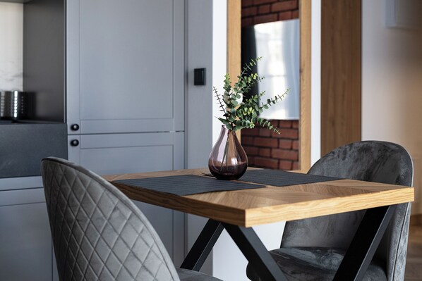 A modern dining area with a wooden table, two cushioned chairs, and a vase with green foliage. - RentPlanet - Apartament Ząbkowska (Warsaw)