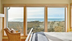 Un dormitorio con un ventanal que da a una playa y dunas.