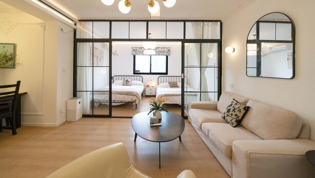 A modern living room with a sofa, a coffee table, and a dining area with chairs. There is a large window with a view of the outside. - YIDU (Nanjing West Road Store) (Shanghai)