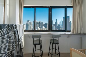 A room with a large window, two black and white checkered barstools, a striped blanket, and a view of a city skyline. - YIDU (Nanjing West Road Store) (Shanghai)
