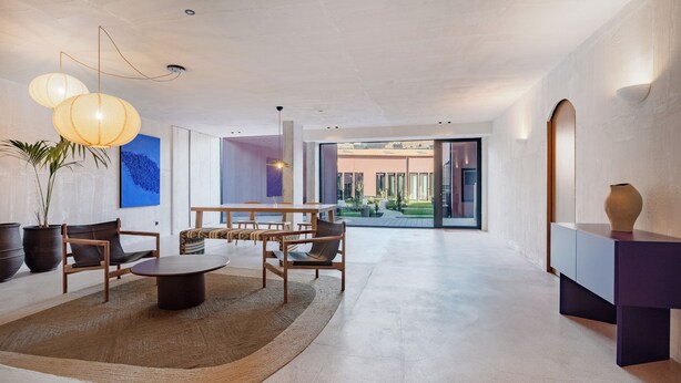 Amplio salón con diseño moderno, que incluye una mesa redonda, dos sillas, un sofá y un gran ventanal con vistas al exterior.