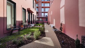Un sendero estrecho bordeado por edificios con ventanas amplias y un pequeño jardín con bancos y plantas en macetas.