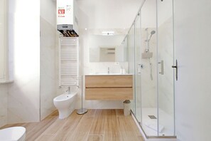Une salle de bain moderne équipée d’un bidet, d’une douche à parois de verre et d’un meuble-lavabo en bois.