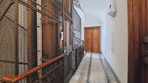 Un pasillo estrecho con piso estampado, una puerta de madera al final y una barandilla metálica a un lado.