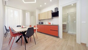 Cocina moderna con encimera de madera, armarios rojos y un microondas. Hay una mesa de comedor con sillas y una puerta de vidrio que da a una zona de ducha.
