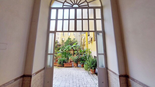 Un arco de entrada da a un patio con macetas y suelo de baldosas.