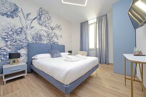 Une chambre à coucher comprenant un lit, des tables de chevet, une lampe et un mur orné d’une fresque florale.