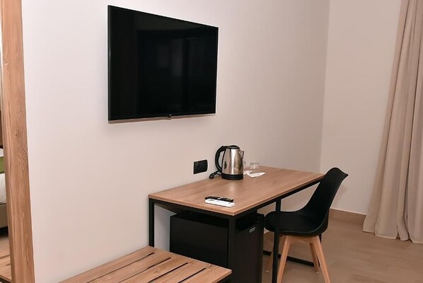 A small room with a wooden table, a black chair, a TV mounted on the wall, and a small black cabinet. - L'escale Hôtel & Spa By 7AV HOTELS (Bni Quolla)