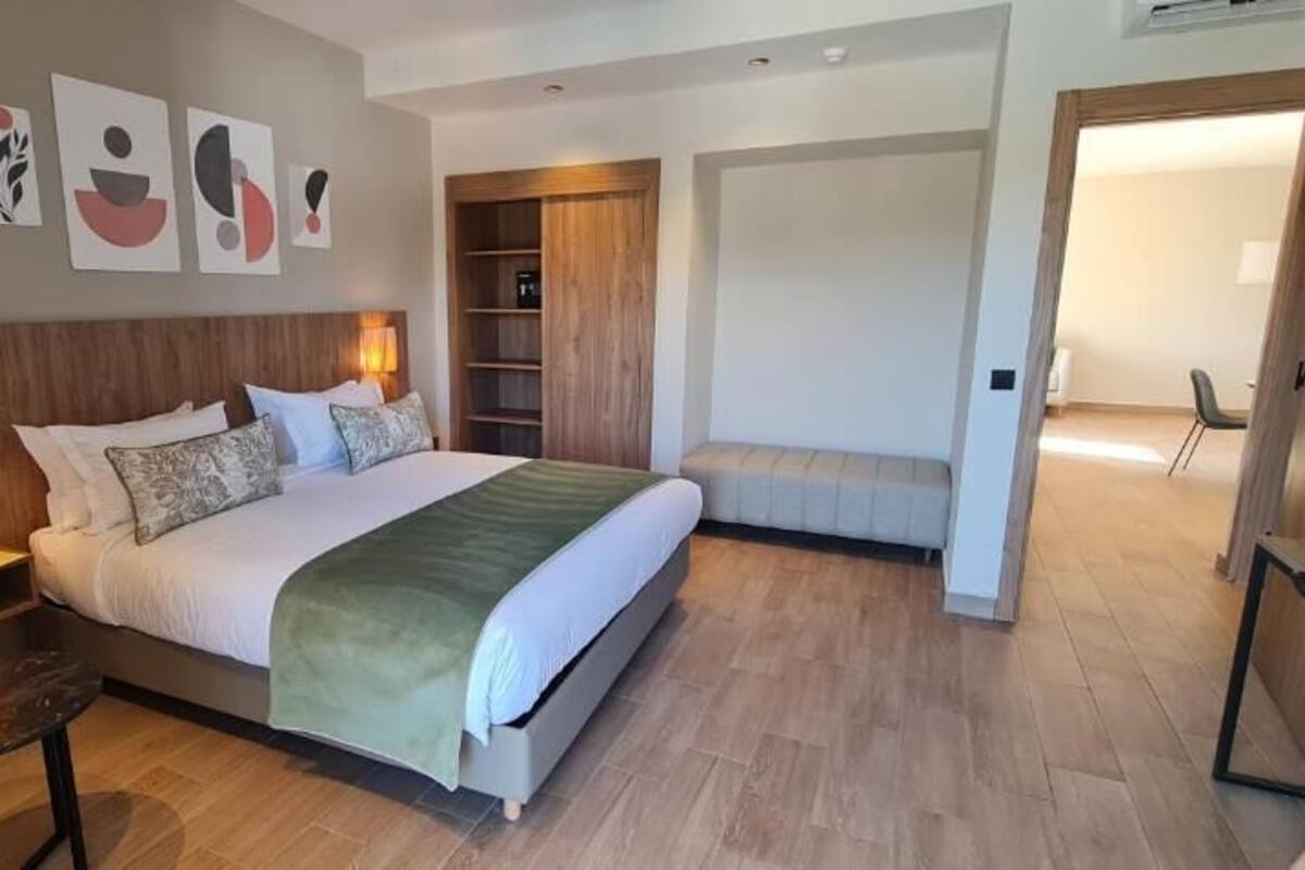A modern hotel room with a large bed, bedside tables, a green armchair, and a wooden wardrobe.