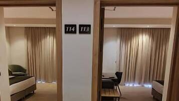 Ett hotellrum med en säng, ett skrivbord och en soffa. Det finns två dörrar, märkta med nummer 114 och 113.