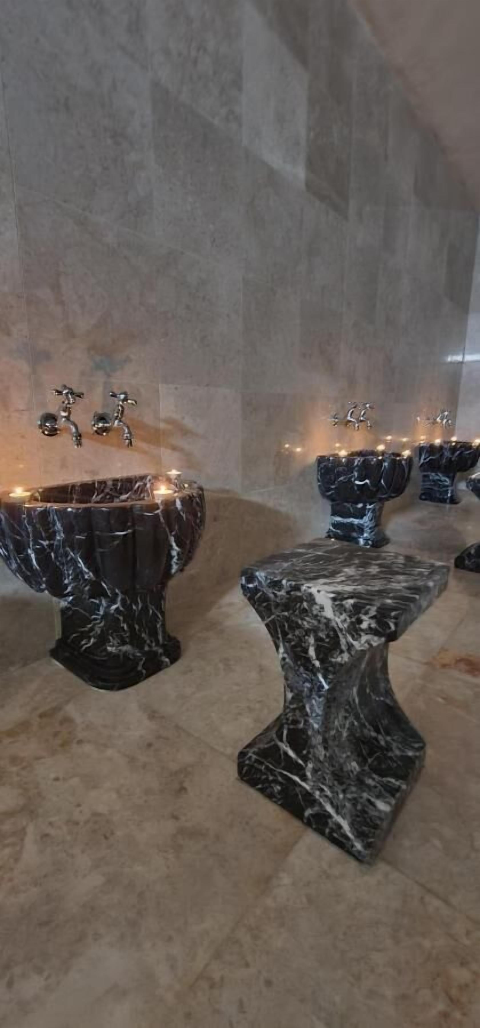 Tinajas de mármol con grifos y velas, frente a una pared de azulejos.