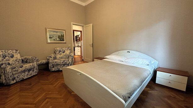 Un dormitorio con cama, una silla, una mesita de noche y una puerta que da a un baño.