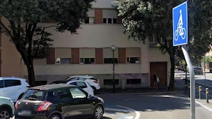 Un estacionamiento con un cartel azul de bicicleta, un edificio con varias ventanas y algunos coches aparcados.