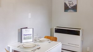 A dining area with a white table, two chairs, and a framed welcome sign. An air conditioner is mounted on the wall. - Westlake Couple`s Cottage (Prince Edward)