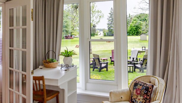 Una habitación con un escritorio blanco, una silla y vistas a un jardín a través de grandes ventanales.