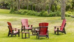 Four Adirondack chairs arranged on a grassy lawn with a forest in the background. - Family friendly duplex (Prince Edward)