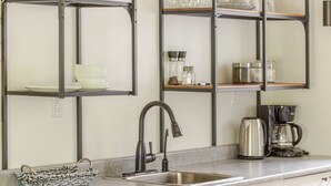 A kitchen with a stainless steel sink, a coffee maker, and shelves with glassware and dishes. - Family friendly duplex (Prince Edward)