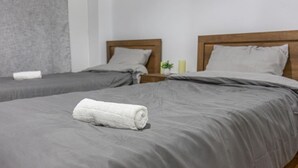 Habitación de hotel con dos camas, ropa de cama gris, cabeceros de madera y una toalla blanca enrollada sobre la cama.
