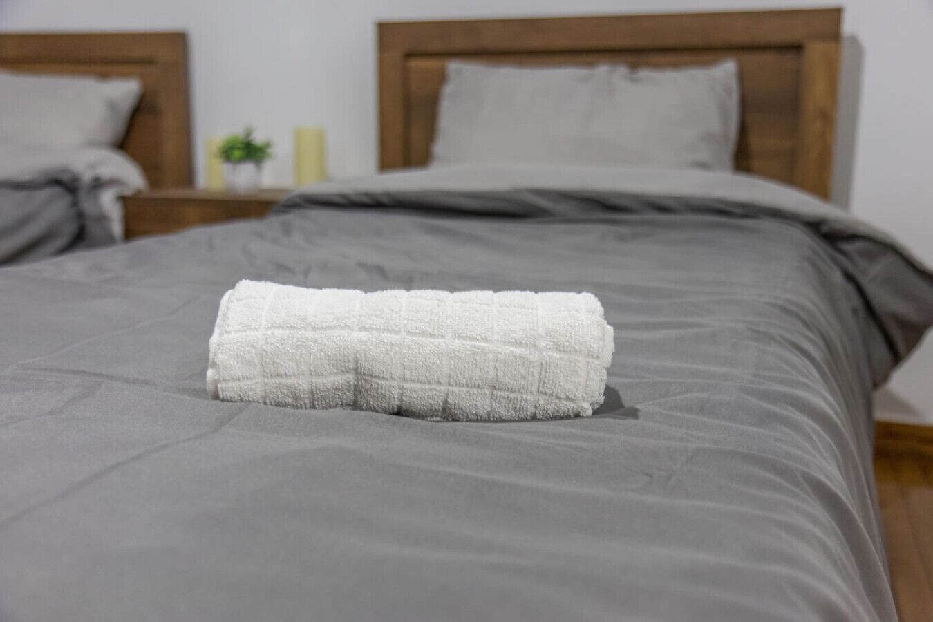 Un lit bien fait, avec une couverture grise et une serviette blanche pliée.