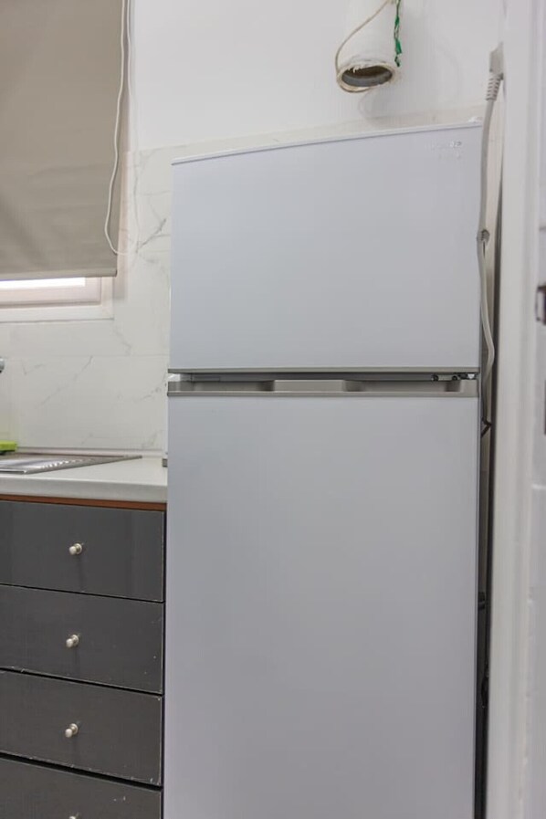 A kitchen with a white refrigerator, a window with blinds, and a black cabinet with drawers.