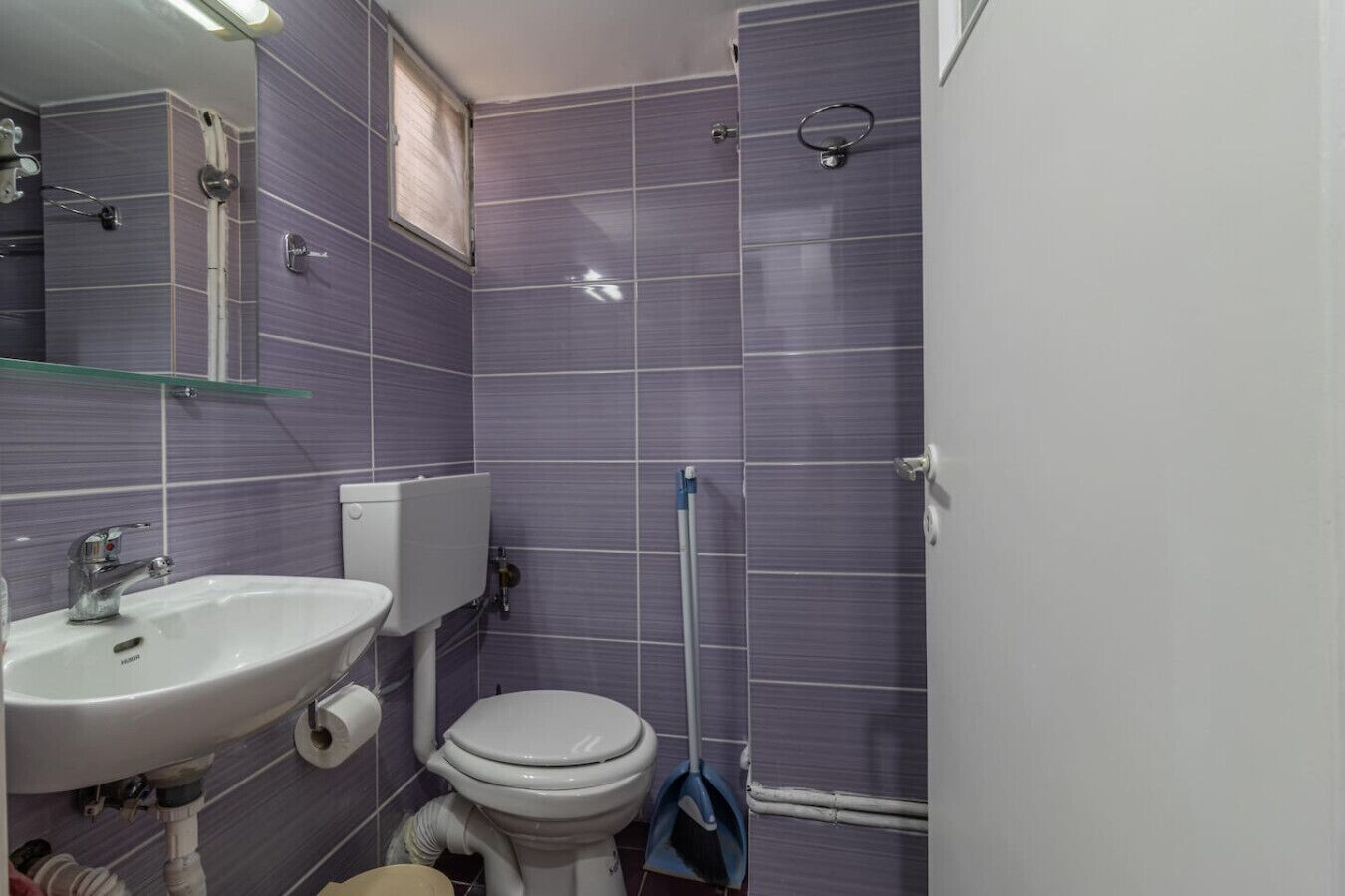 Et badeværelse med en hvid vask, toilet og en glashylde over vasken.