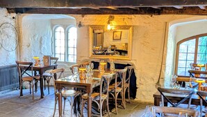 A rustic dining area with wooden tables and chairs, stone flooring, and a large mirror on the wall. - Old Mill Salisbury (Salisbury)