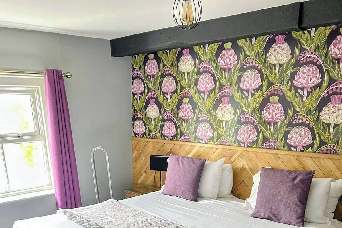 A hotel room with a large bed, a wooden headboard, and a floral wallpaper design.