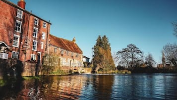 A historic building with a brick facade and a thatched roof, located beside a calm river.