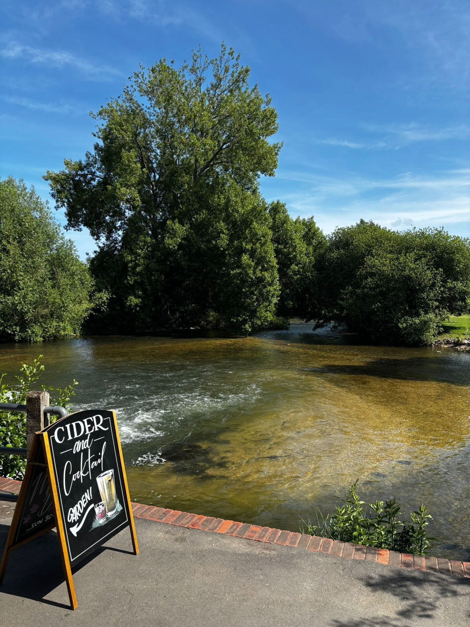 Letrero que anuncia sidra y jardín, con un río y árboles al fondo.
