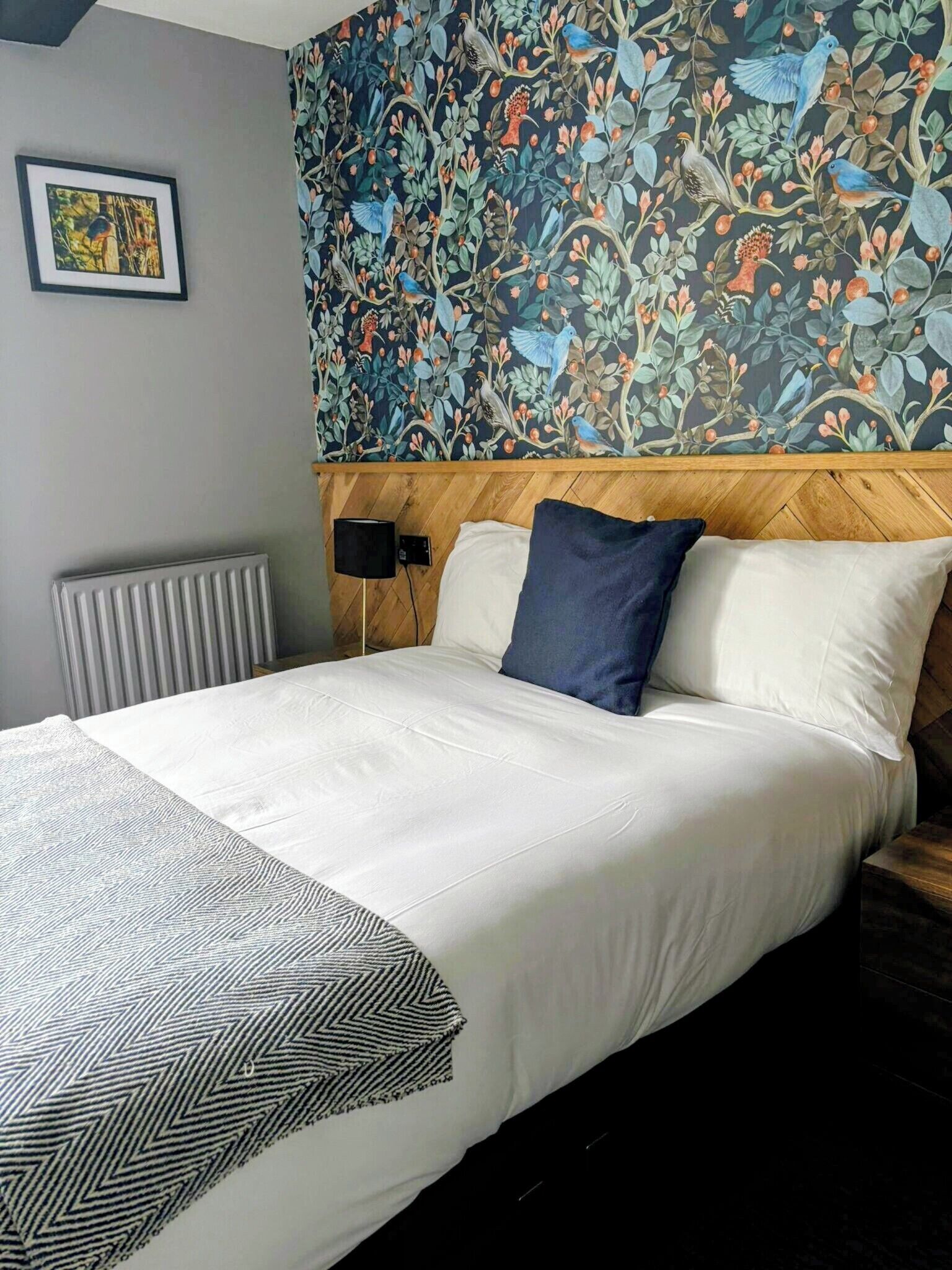 A hotel room with a large bed, a wooden headboard, a radiator, and a wall with a floral wallpaper.