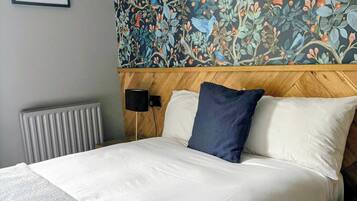 A hotel room with a large bed, a wooden headboard, a radiator, and a wall with a floral wallpaper.