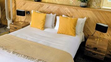 Un letto rifatto con lenzuola bianche e due cuscini color senape, affiancato da due comodini in legno con lampade nere.