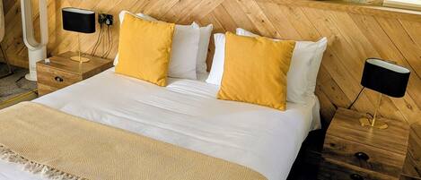 A neatly made bed with white linens and two mustard-colored pillows, flanked by wooden nightstands with black lamps.