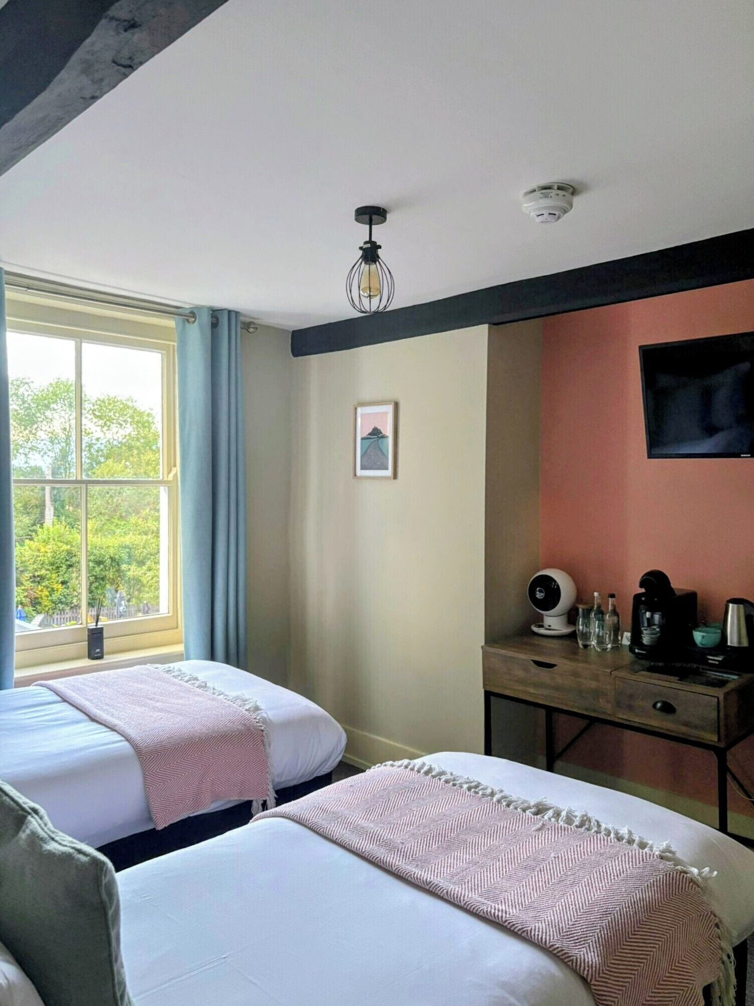 A hotel room with two beds, a desk with a coffee maker, a TV, and a window with curtains.