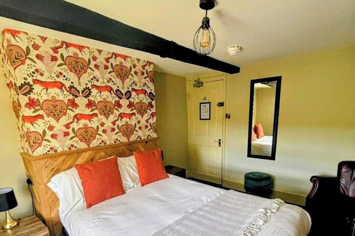 A neatly arranged bedroom with a large bed, a wooden headboard, a bedside table, a mirror, and a hanging light fixture.