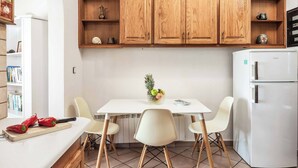 A kitchen with wooden cabinets, a white refrigerator, a dining table with chairs, and a cutting board with red peppers. - Villa Jasmin Nissaki (Nisaki)