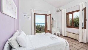 A bedroom with a bed, a desk, and a view of the outdoors. - Villa Jasmin Nissaki (Nisaki)