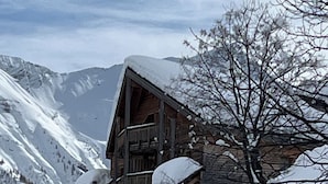 Un chalet en bois à plusieurs étages, doté de balcons, qui se dresse sur fond de montagnes enneigées.