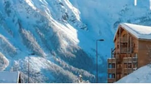 Un chalet en bois, dont le toit est recouvert de neige, se dressant sur un fond de montagnes enneigées.