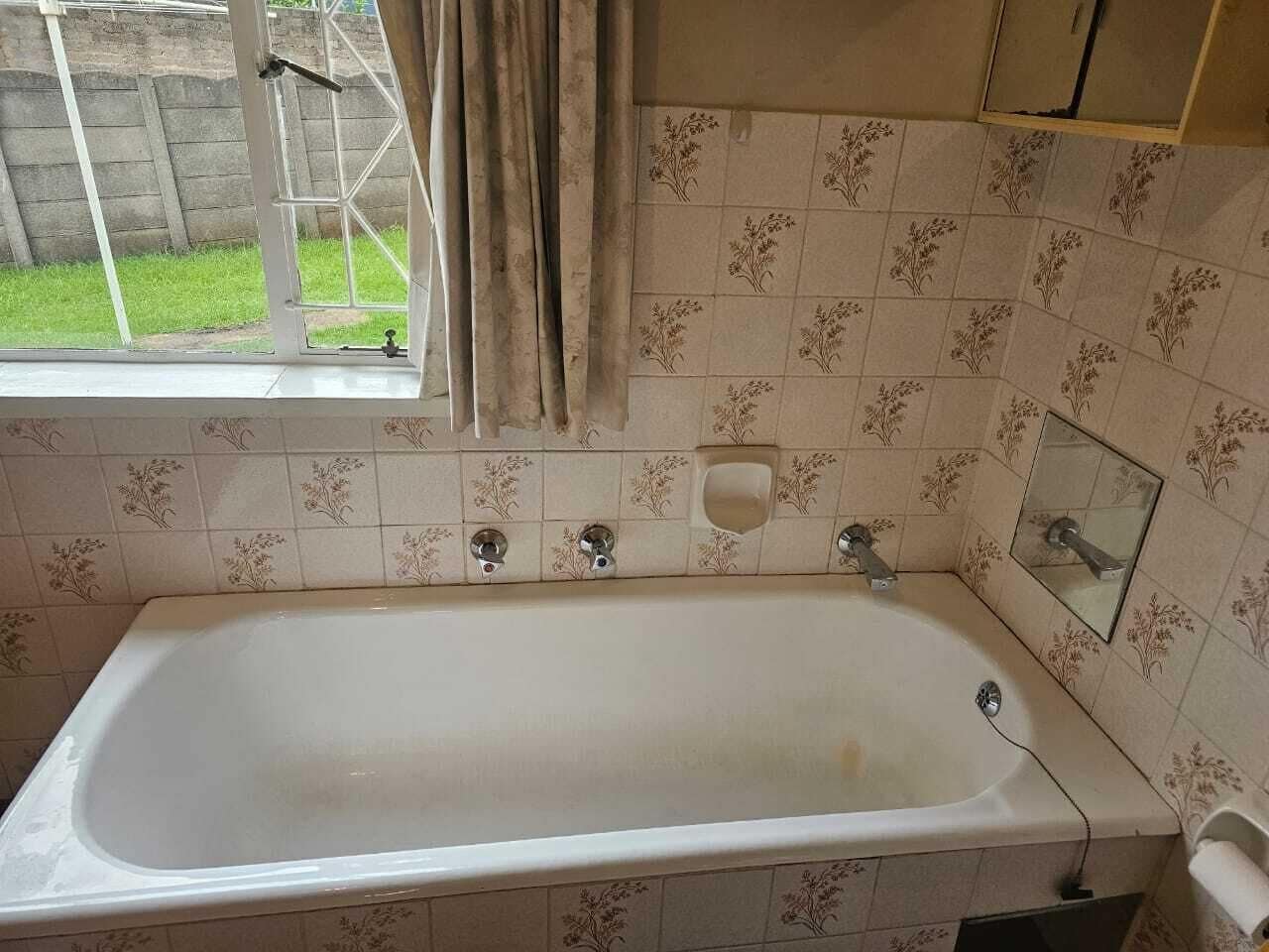 Casa de banho com banheira, janela com cortinas e azulejos estampados.