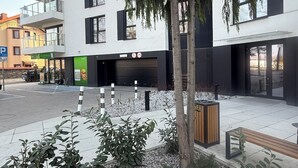 A modern building with multiple floors, a parking area, and a small garden with plants and gravel.