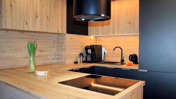 A modern kitchen with wooden cabinetry, a built-in stove, a coffee machine, and a sink.