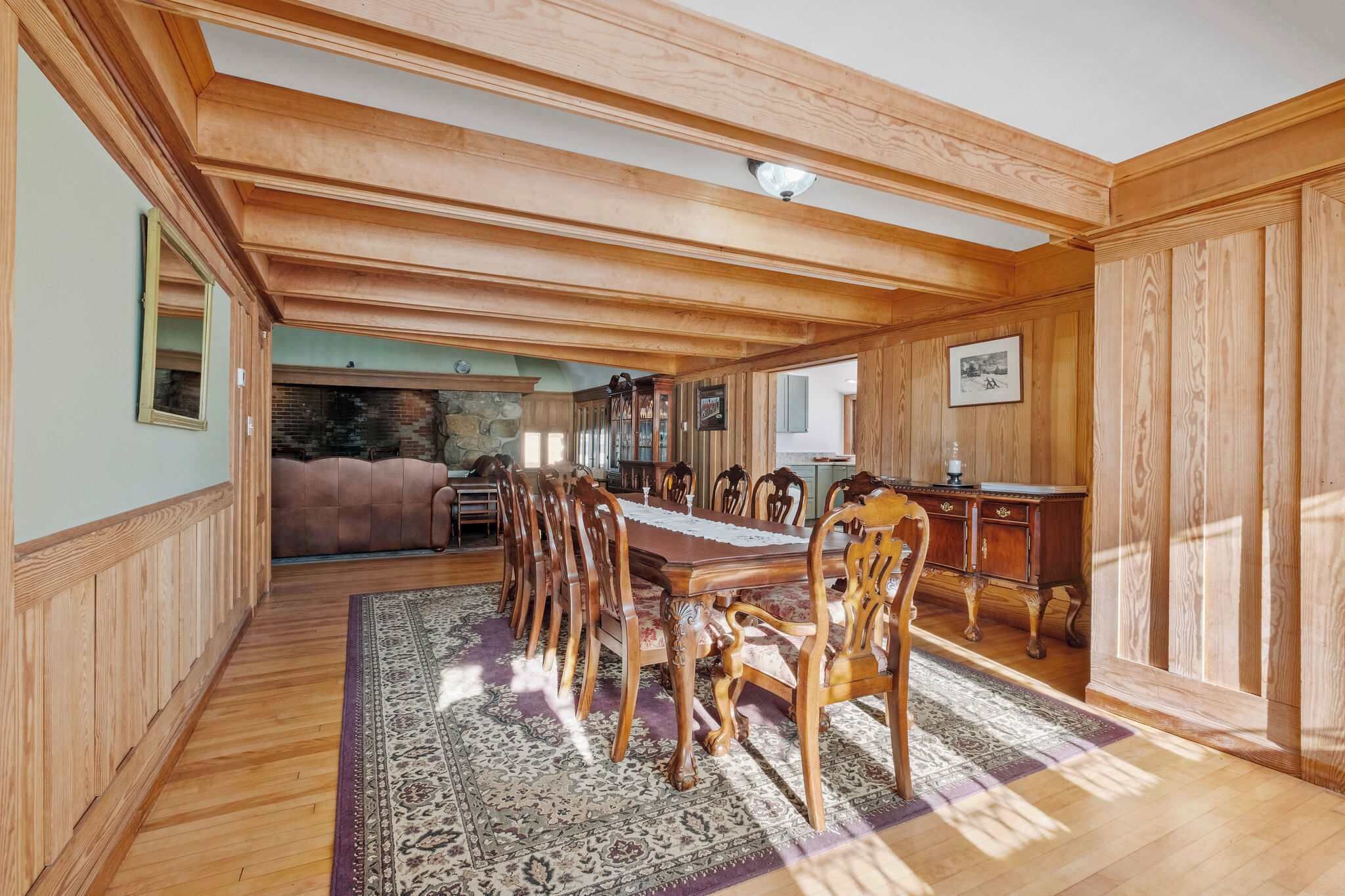 Un comedor con una mesa de madera larga y sillas, un tapete estampado y paneles de madera en las paredes y el techo.