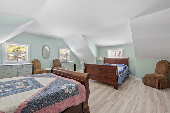 A bedroom with a large bed, two smaller beds, a dresser, a chair, and a window with a view.