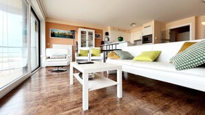 En moderne stue med en hvid sofa, et sofabord og et spiseområde med et køkken i baggrunden.