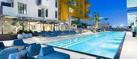 A swimming pool with lounge chairs and umbrellas, surrounded by modern buildings.
